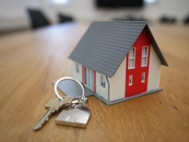 miniature house with a key beside it conceptualizing real estate